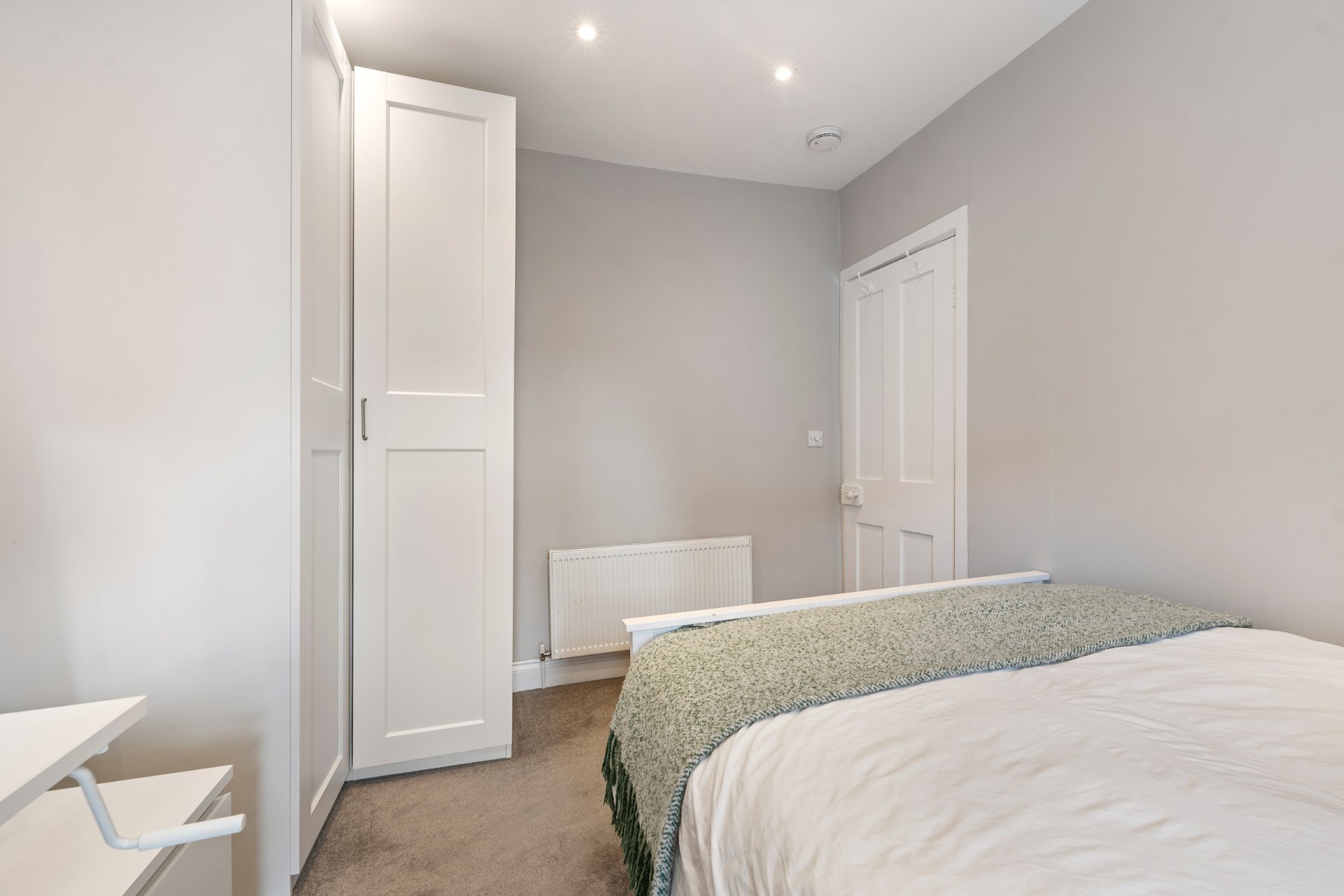 A bright double bedroom with a fitted wardrobe and warm grey tones.