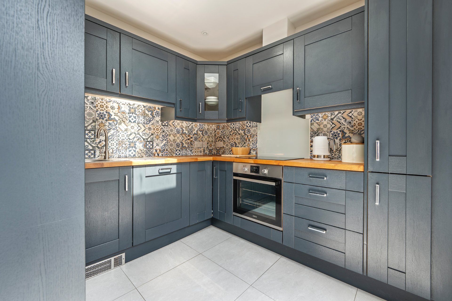 A corner of the navy shaker kitchen with oak worktops and patchwork tiling.