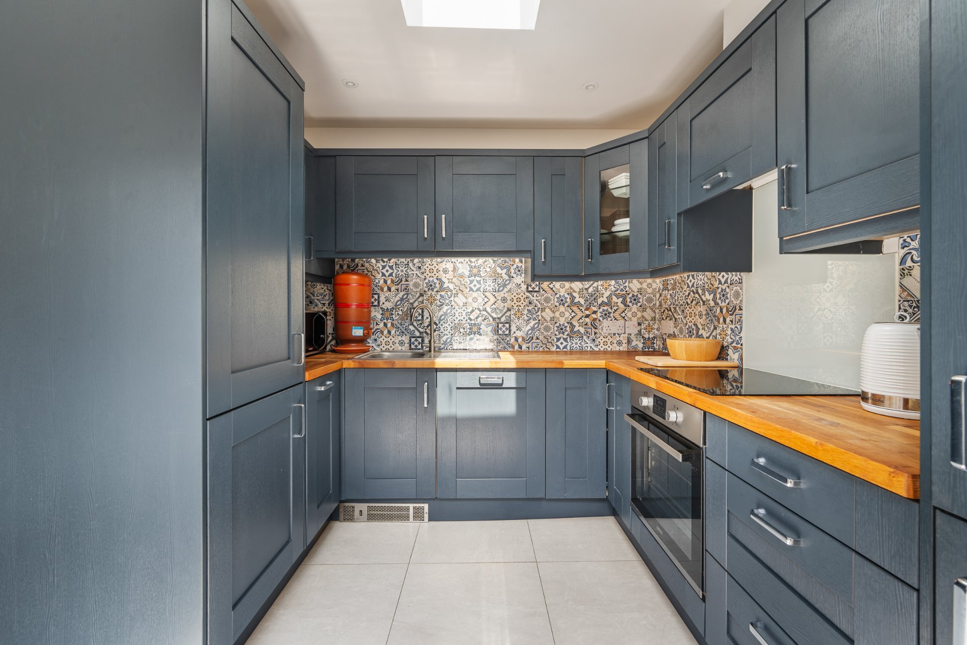The navy kitchen under a skylight, with oak worktops and a patterned splashback.