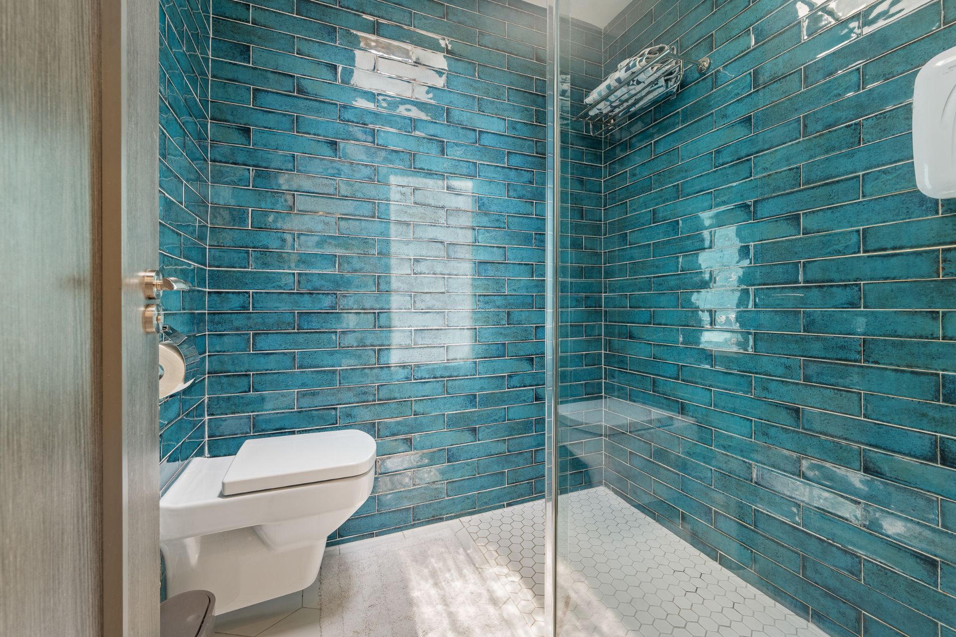 The walk-in shower and wall-hung WC, finished in glossy teal tiles.